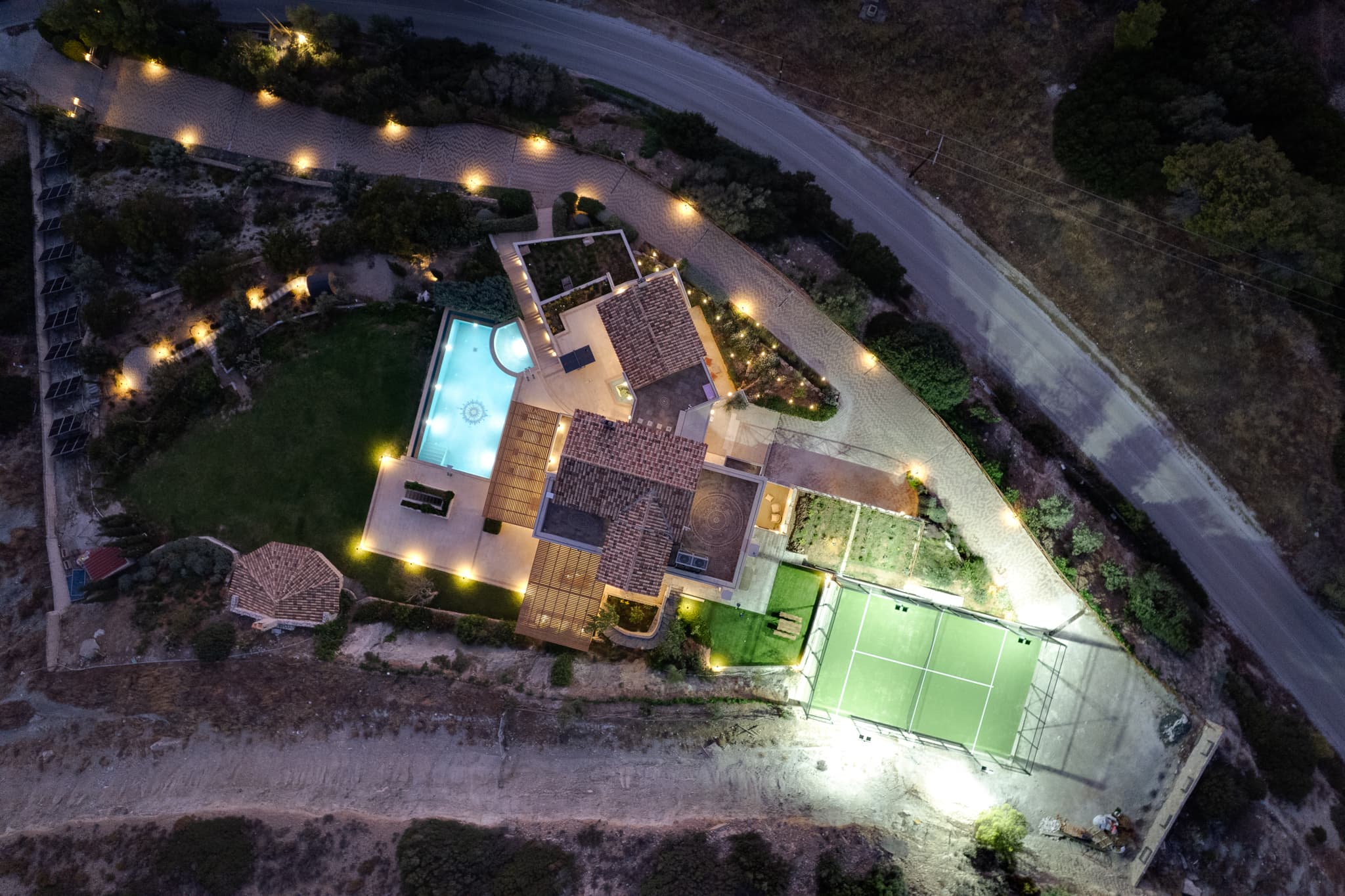 Aerial view of the estate at dusk with the pool and the padel court lit
